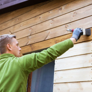 man painting exterior of cabin